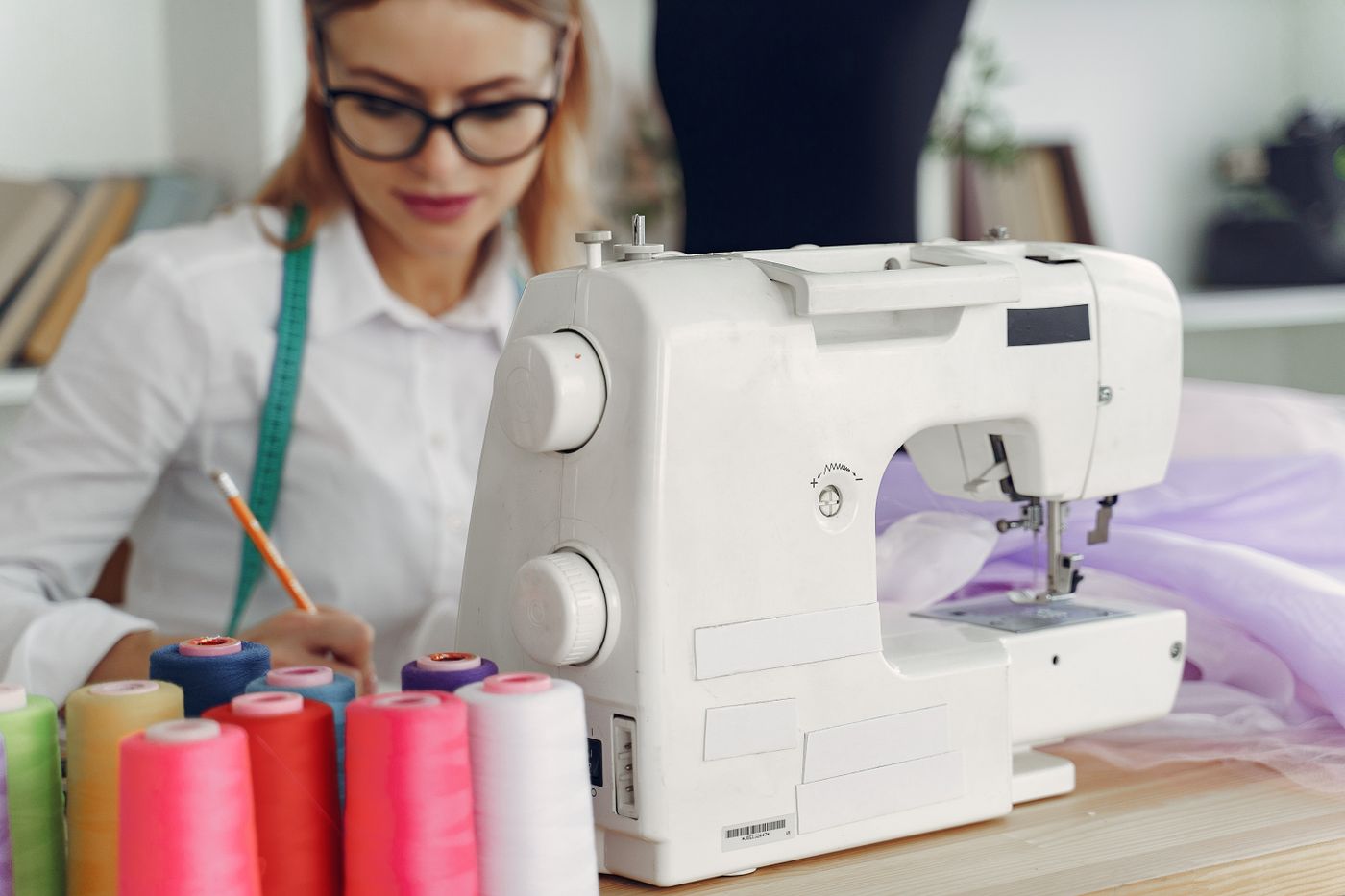 A sewing machine, coloured thread, and a dressmaker at a work table